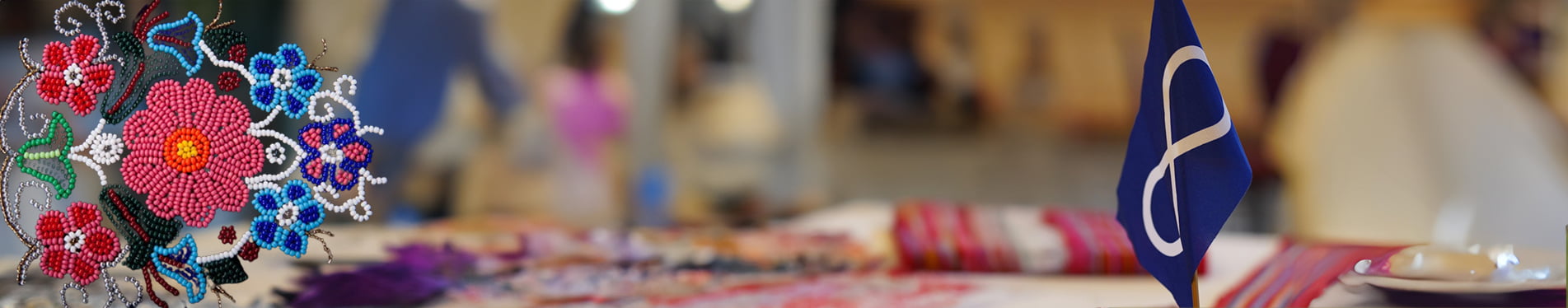 Header With Beadwork Indigenous blue infinity symbol flag on a table with a traditional metis red river sash